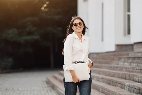 Retrato de una chica de moda vestida con vaqueros y camisa blanca que sostiene el ordenador portátil, trabajador independiente, dama de negocios, concepto de poder de la mujer —  Fotos de Stock