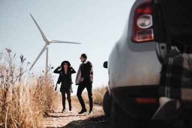 Arka planda elektrikli rüzgar türbini jeneratörüyle Saha Yolu 'nda Yolculuk Yapan Mutlu Seyahat Çifti