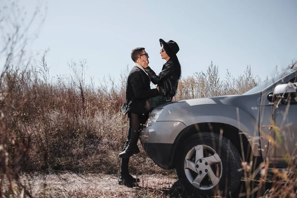 Retrato de feliz pareja viajera vestida con ropa negra con estilo disfrutando de un viaje en coche en el camino de campo, concepto de vacaciones —  Fotos de Stock