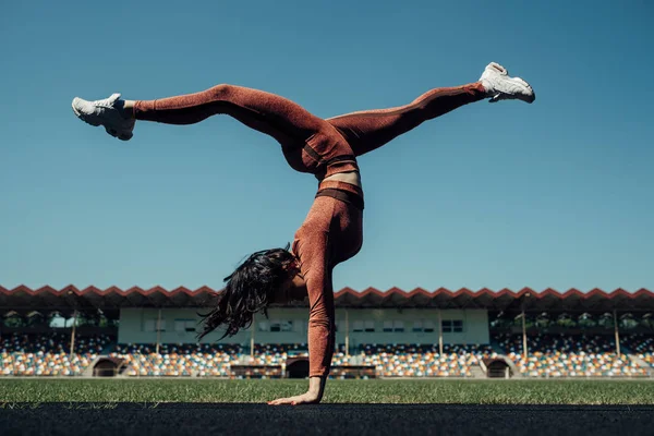 Retrato de una chica deportiva vestida con ropa deportiva de moda haciendo ejercicio y volteretas en el estadio de la ciudad, concepto de estilo de vida saludable — Foto de Stock