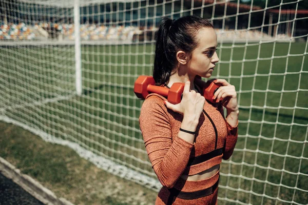 Retrato de una chica deportiva vestida con ropa deportiva haciendo ejercicio con mancuerna y entrenamiento en el estadio de la ciudad, concepto de estilo de vida saludable — Foto de Stock