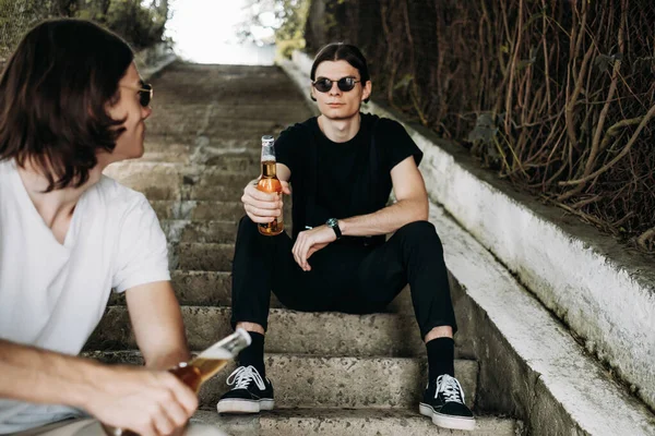 Два стильных брата-близнеца веселятся, выпивая пиво на лестнице — стоковое фото