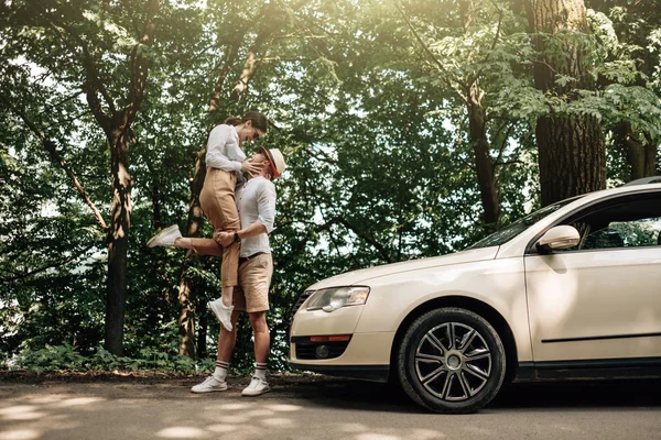 Joven pareja feliz vestida como en camiseta blanca divirtiéndose cerca del coche, fin de semana fuera de la ciudad, días festivos y concepto de viaje por carretera — Foto de Stock