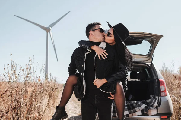 Pareja feliz viajando disfrutando de un viaje en coche en la carretera de campo con generador de energía de turbina eólica eléctrica en el fondo —  Fotos de Stock