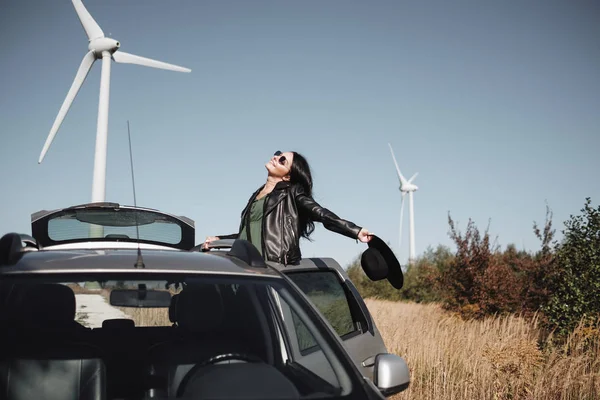 幸せな旅行の女の子背景に電動風力タービン発電機でフィールド道路上の車の旅を楽しむ — ストック写真