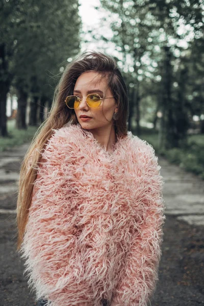Πορτρέτο του ένα κομψό κορίτσι σε ροζ παλτό και μοντέρνα κίτρινο γυαλιά ηλίου που ποζάρει στην οδό — Φωτογραφία Αρχείου