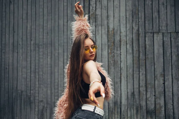 Retrato de cerca de una chica elegante con abrigo rosa y gafas de sol amarillas modernas posando en la calle — Foto de Stock
