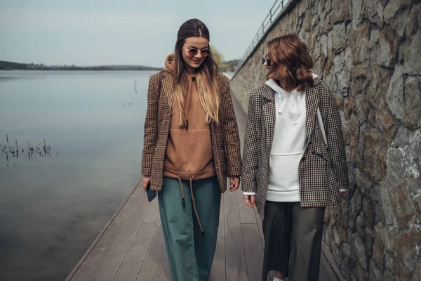 Retrato de dos chicas de moda, Mejores amigos al aire libre, Usando chaqueta elegante, Caminando cerca del lago —  Fotos de Stock