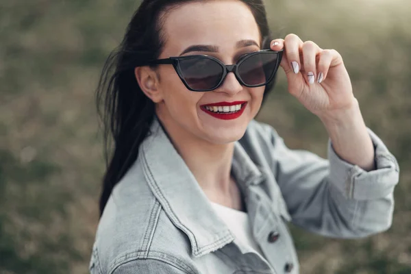 Vacker brunett flicka i solglasögon vita byxor och jeans jacka, rött läppstift — Stockfoto