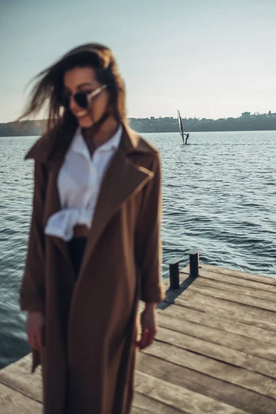 Hermosa joven con estilo chica de abrigo caminando en la playa de primavera al atardecer —  Fotos de Stock