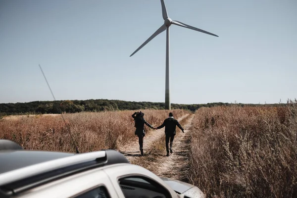 幸せな旅行カップル背景に電動風力タービン発電機でフィールドロードで車の旅を楽しむ — ストック写真