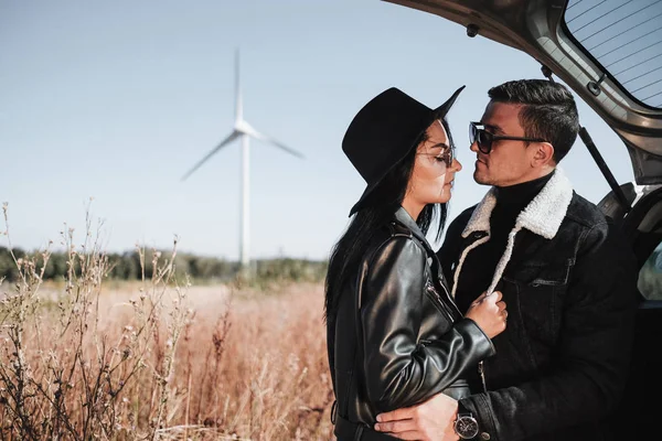 Felice coppia di viaggio godendo di un viaggio in auto sulla strada di campo con generatore di energia elettrica a turbina eolica sullo sfondo — Foto Stock