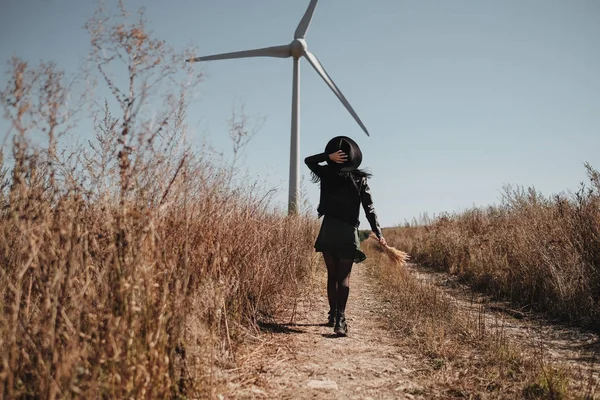 Happy Traveling Girl Enjoying a Trip on the Field Road with Electric Wind Turbine Power Generator on the Background
