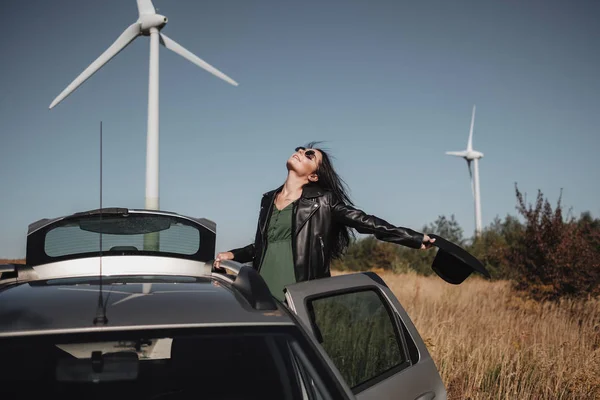 Happy Traveling Girl Enjoying a Car Trip on the Field Road with Electric Wind Turbine Power Generator on the Background — Stock Photo, Image