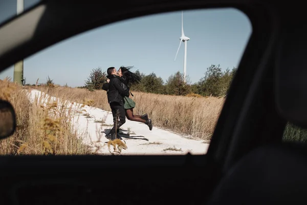 Casal viajante feliz desfrutando de uma viagem de carro na estrada de campo com gerador de energia elétrica turbina eólica no fundo — Fotografia de Stock