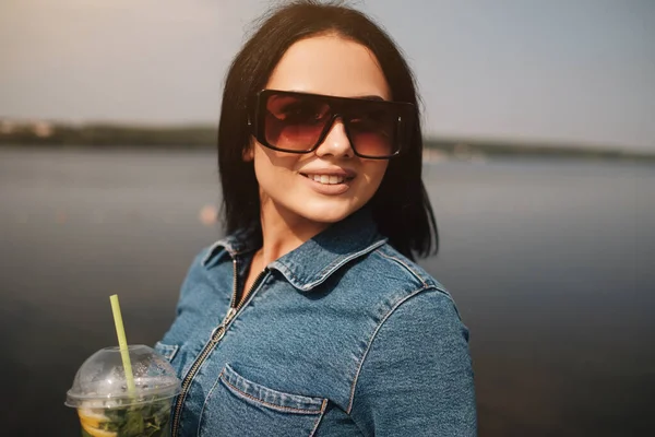 Een mooie Brunette meisje gekleed in jeans Overalls drankjes cocktail — Stockfoto