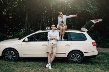 Beyaz tişörtlü genç mutlu çift arabanın yanında eğleniyor, hafta sonu şehir dışında, tatiller ve yolculuk konsepti.