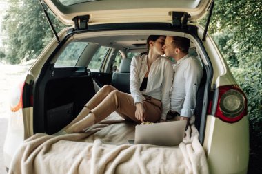 Genç, mutlu, beyaz tişörtlü bir çift. Araba bagajında dizüstü bilgisayar ve patlamış mısırla oturuyor. Hafta sonu şehrin dışında, tatillerde ve yolculukta.