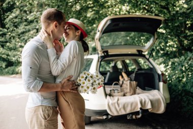 Beyaz tişörtlü genç mutlu çift arabanın yanında eğleniyor, hafta sonu şehir dışında, tatiller ve yolculuk konsepti.