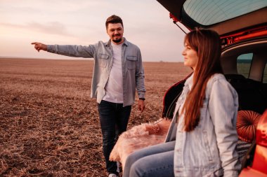 Beyaz Gömlekli ve Kot Giyen Genç Mutlu Çift Yeni Araba Bagajlarında Oturuyor, Sahada Güzel Günbatımı, Tatil ve Seyahat Konsepti
