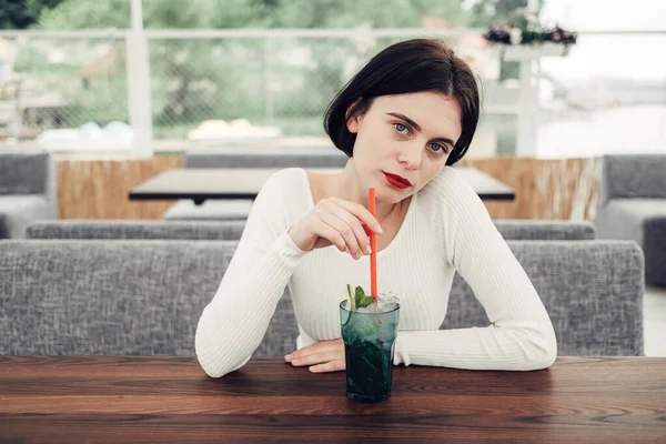 Närbild Porträtt av vacker Brunett flicka i vit tröja Sitter i Café och drinkar cocktail — Stockfoto