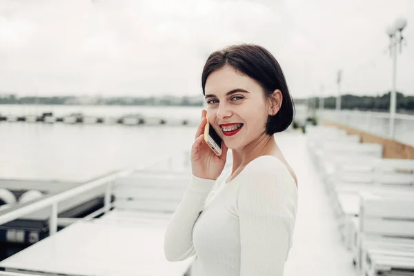 Närbild Porträtt av vacker Brunett flicka i vit tröja glad leende med tandställning talar på mobilen — Stockfoto