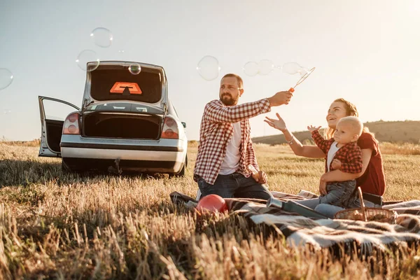Happy Young Family Mom and Dad with Their Little Son Enjoying Summer Weekend Picnic on the Car Outside the City, Play with Bubbles — Stok Foto