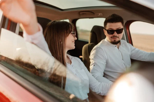 Young Happy Couple Dressed Alike in White Shirt and Jeans Enjoying Road Trip at Their New Car, Beautiful Sunset on the Field, Vacation and Travel Concept — 스톡 사진