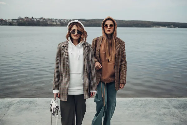 Портрет двух девушек из моды, лучшие друзья на открытом воздухе, в стильной куртке, прогулки у озера — стоковое фото
