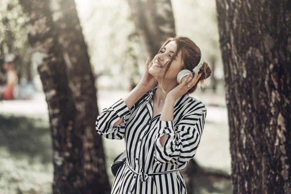 Outdoor Summer Portrait of Young Beautiful Girl in White Striped Stylish Dress Listens Music in Headphones — Stock Photo, Image