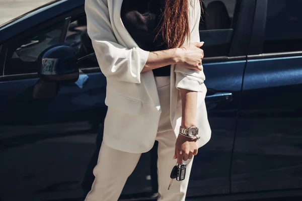 Chica con estilo de moda en traje blanco posando cerca del coche azul y sostiene las llaves en la mano — Foto de Stock