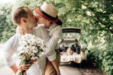 Beyaz tişörtlü genç mutlu çift arabanın yanında eğleniyor, hafta sonu şehir dışında, tatiller ve yolculuk konsepti.