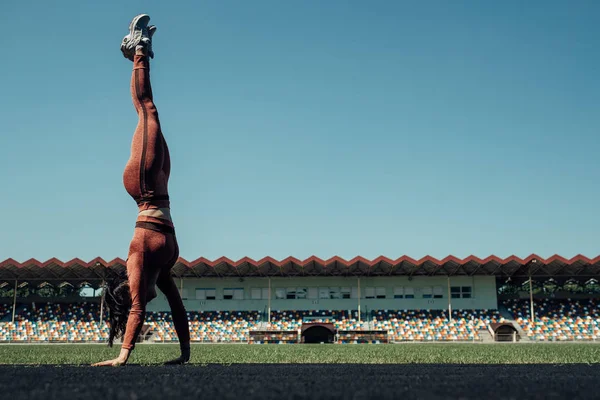 Retrato de una chica deportiva vestida con ropa deportiva de moda haciendo ejercicio y volteretas en el estadio de la ciudad, concepto de estilo de vida saludable — Foto de Stock