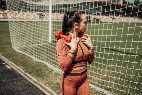 Retrato de una chica deportiva vestida con ropa deportiva haciendo ejercicio con mancuerna y entrenamiento en el estadio de la ciudad, concepto de estilo de vida saludable — Foto de Stock
