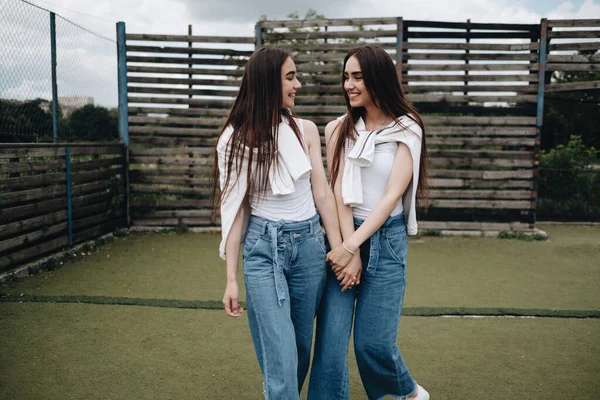 Retrato de dos hermanas gemelas morenas jóvenes vestidas como en pantalones vaqueros y camiseta blanca, mejor concepto de amigos para siempre — Foto de Stock