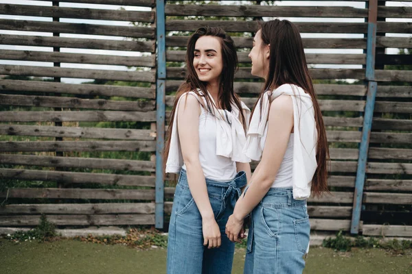 Retrato de dos hermanas gemelas morenas jóvenes vestidas como en pantalones vaqueros y camiseta blanca, mejor concepto de amigos para siempre —  Fotos de Stock