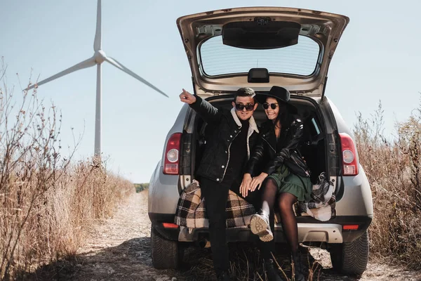 幸せな旅行のカップル電動風力タービン発電機でフィールド道路のトランクに座って車の旅を楽しむ — ストック写真
