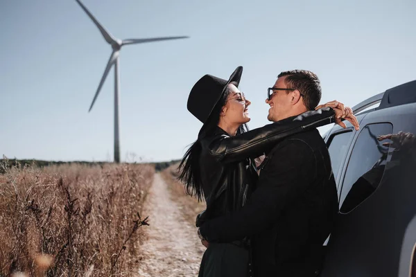 Casal viajante feliz desfrutando de uma viagem de carro na estrada de campo com gerador de energia elétrica turbina eólica no fundo — Fotografia de Stock