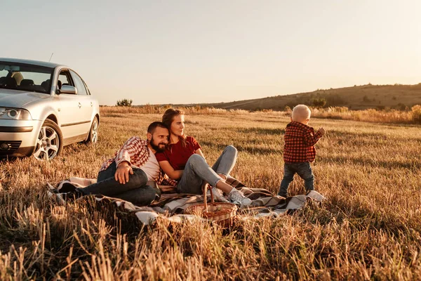 Glad ung familj mamma och pappa med sin lilla son Njuter av sommar helg picknick på bilen utanför staden i fältet på soliga dagen solnedgång, semester och väg resa koncept — Stockfoto