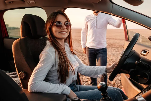 Young Happy Couple Dressed Alike in White Shirt and Jeans Enjoying Road Trip at Their New Car, Beautiful Sunset on the Field, Vacation and Travel Concept — 스톡 사진