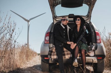 Elektrikli Rüzgâr Türbini Güç Üreteç 'iyle Tadını Çıkaran Mutlu Seyahat Çifti Saha Yolundaki Bagajda Oturuyor