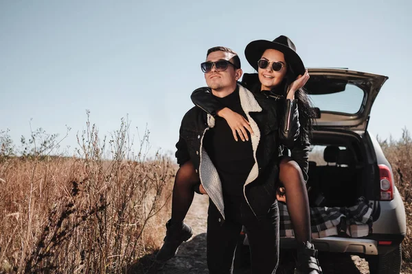 Boldog utazó pár öltözött fekete elegáns ruhák Élvezi a Car Trip a Field Road, nyaralás koncepció — Stock Fotó