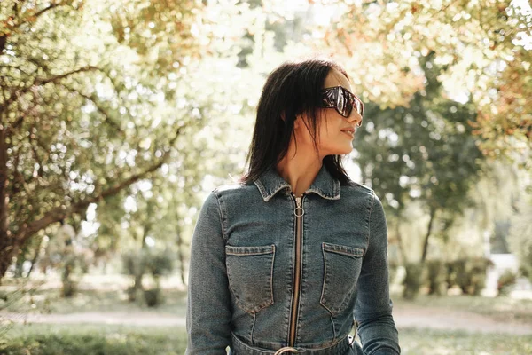 Close Up Portrét jedné krásné brunety dívka oblečená v džínách džínové kombinézy procházky v podzimním parku — Stock fotografie