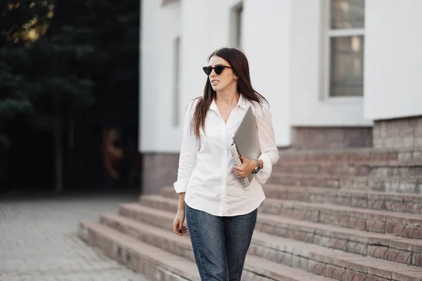 Retrato de una chica de moda vestida con vaqueros y camisa blanca que sostiene el ordenador portátil, trabajador independiente, dama de negocios, concepto de poder de la mujer — Foto de Stock