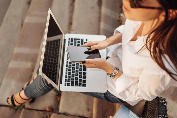 Retrato de uma menina na moda vestida de jeans e camisa branca trabalhando no laptop, trabalhador freelance, senhora de negócios, conceito de poder da mulher — Fotografia de Stock
