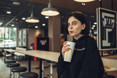 Ternopil, Ukrayna - 25 Mayıs 2019: Siyah Kazaklı Güzel Esmer Kız 'McDonalds' ta Coca-Cola İçiyor