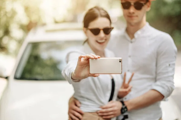 Joven Pareja Feliz Vestido Igual en Camiseta Blanca Sosteniendo Smartphone Cerca del Coche, Fin de Semana Fuera de la Ciudad, Vacaciones y Concepto de Viaje por Carretera — Foto de Stock