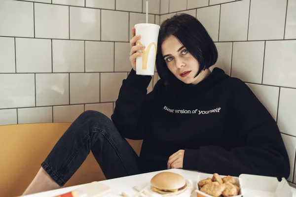 TERNOPIL, UCRAINA - 25 MAGGIO 2019: Bella ragazza bruna in Pullover nero con testo "Best Version of Yourself" beve Coca-Cola in McDonalds — Foto Stock