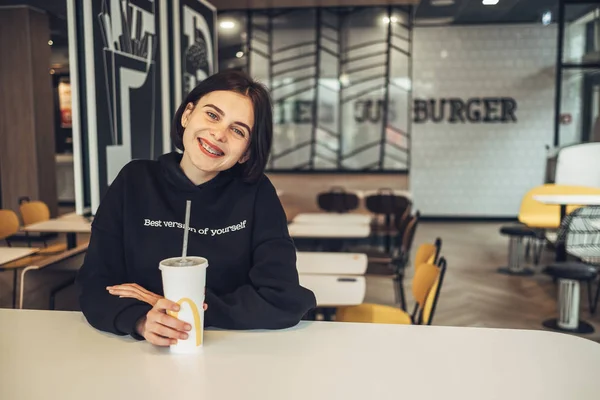 Ternopil, Ukraina - 25 maj 2019: Beautiful Brunette Girl in Black Pullover with Text '' Best Version of Yourself 'Drinks Coca-Cola in Mcdonalds — Stockfoto