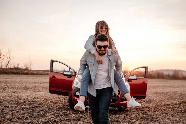 Молода пара вдягнена так само, як у білій сорочці та джинсах, які насолоджуються дорожньою подорожжю на своїй новій машині, прекрасним заходом сонця на полі, відпусткою та подорожньою концепцією — стокове фото